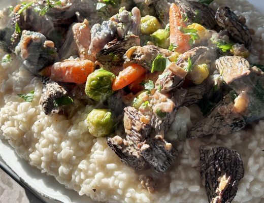 "Risotto cremoso alla parmigiana con funghi Morilles e verdure colorate saltate al burro, servito in un elegante piatto bianco su sfondo rustico."